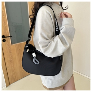 Side view of black crescent shoulder bag with FASHION strap and plush charm