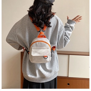 Détail du mini sac à dos en toile avec bretelles orange et corps gris sur modèle