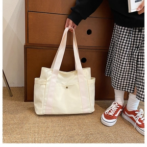 Detail of off-white canvas tote bag featuring side pockets and a metal snap closure
