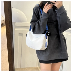 Detail of white PU crossbody bag with blue fabric strap and cute black plush charm