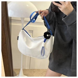 Close-up of a white crescent bag featuring a blue strap and black plush ball accessory