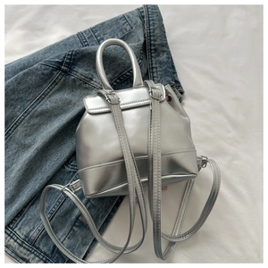 Overhead view of a small silver metallic backpack placed on blue denim and white fabric