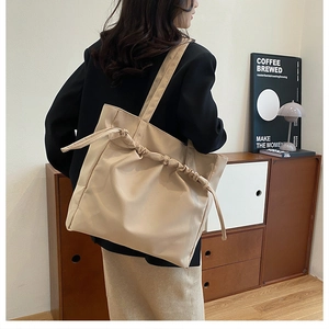 Detail of a beige canvas tote bag with drawstring pleats worn by a model in a cozy setting