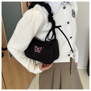 Détail de broderie papillon rose sur sac à bandoulière noir avec sangle froncée