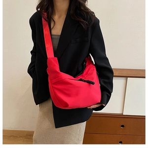 Detailed view of a bright red Oxford cloth crossbody bag paired with a black suit jacket