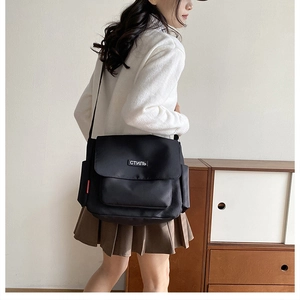 Detail of black canvas messenger bag with white embroidery and red decorative tag