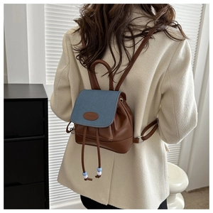 Detail view of mini denim backpack with brown leather strap and brand logo patch