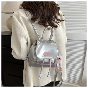 Detail of silver metallic mini backpack with pink logo plaque and plush monster keychain