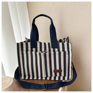 Detail of blue and white striped canvas tote with front pockets and brown leather tag
