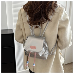 Detail of silver shiny mini backpack with pink emblem and decorative colorful beads