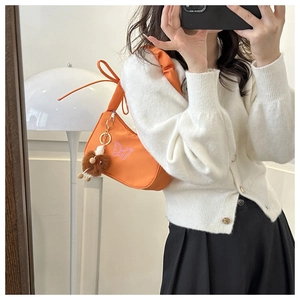 Détail du sac hobo orange avec broderie papillon rose et pendentif en peluche marron