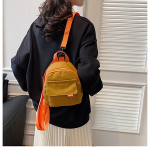 Vue détaillée du mini sac à dos en toile jaune moutarde avec bandoulière orange sur modèle