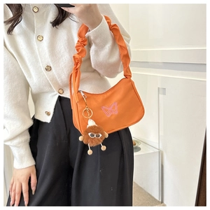 Détail d'un sac à bandoulière en nylon orange avec broderie papillon et breloque