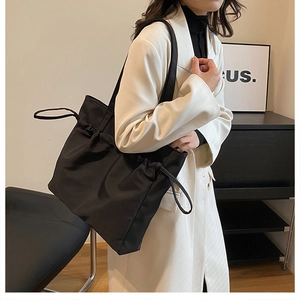 Detail of black nylon tote bag with drawstring texture worn on white coat by a model