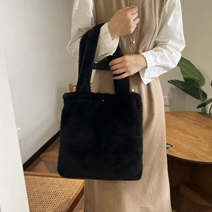 Close-up of a soft black plush tote bag held by a model in a cozy indoor setting