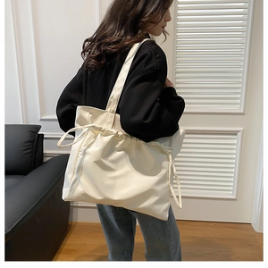 Detail of white knit tote bag featuring side drawstrings and soft pleated texture