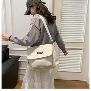 Close-up of a white canvas messenger bag with a stylish black label worn by a model