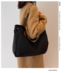Detail of black canvas tote bag showing brown leather buckle and wide shoulder strap