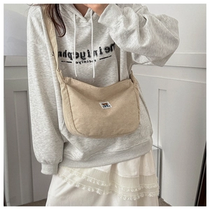 Detail of beige corduroy crescent bag with bear tag worn over a grey hoodie outfit