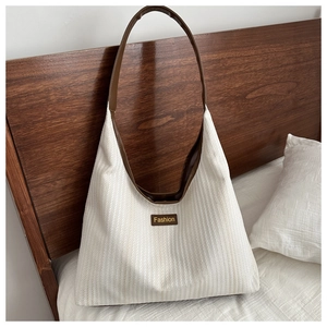 Detail of cream canvas tote bag showing striped fabric texture and brown leather logo tag