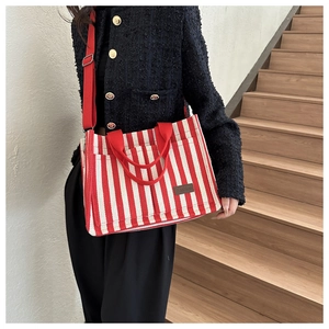 Detail of red and white striped canvas tote bag with adjustable shoulder strap and leather patch