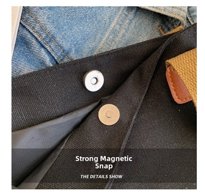 Close-up of the strong magnetic silver buckle and leather trim on the black canvas bag