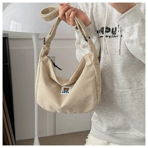 Detailed shot of cream corduroy dumpling bag with adjustable strap and bear label