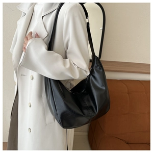 Détail du sac hobo en cuir noir avec texture et bandoulière réglable sur un trench blanc
