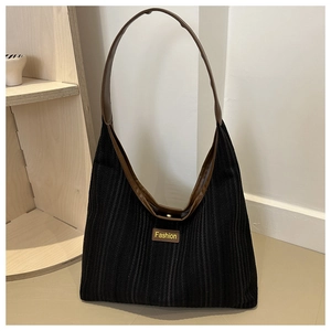 Detail of black corduroy tote bag featuring leather handles and a brown fashion label