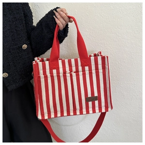 Close-up of red and white striped canvas tote bag with dual straps and leather patch