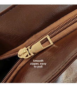 Detail of smooth gold metal zipper and textured dark brown leather on tote bag