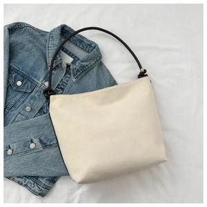 Flat lay of a matte cream tote bag with black tubular shoulder straps and denim jacket