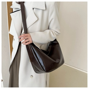 Détail d'un sac hobo en cuir marron foncé porté avec un trench blanc pour un style chic