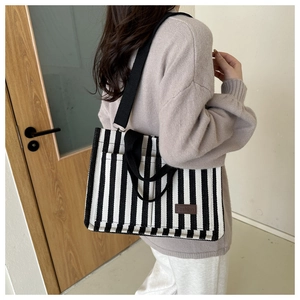 Side view of striped canvas tote bag with black wide strap and leather fashion label