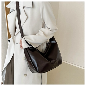 Grand sac à bandoulière marron foncé brillant porté par un mannequin en trench blanc