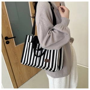 Detail of striped canvas tote bag showing black fabric straps and a leather fashion tag