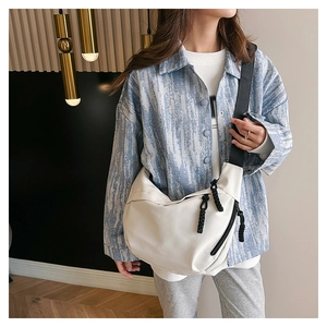Detail of a minimalist cream nylon crossbody bag featuring a black woven zip pull and wide strap