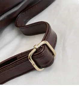 Detail of dark brown leather strap with polished gold buckle and precision stitching