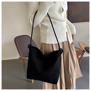 Model wearing a large black matte suede bucket bag with decorative shoulder strap knots