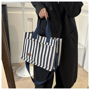 Detail of navy striped canvas tote bag showing the leather logo and sturdy shoulder strap