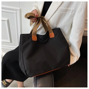Detail of black canvas tote bag showing brown straps and leather trim on a model