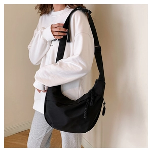 Detail of black crescent crossbody bag with braided zipper pull and wide adjustable strap