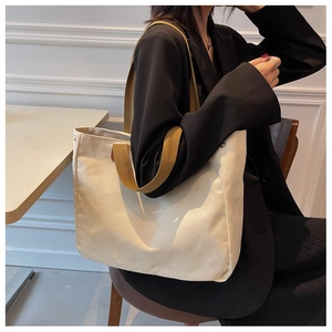 Detailed view of canvas tote bag with brown handles carried by a model in a black blazer