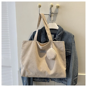 Detailed close-up of corduroy tote bag with small round coin purse and logo tag