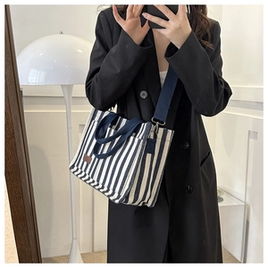Detail of canvas tote with blue stripes, featuring dark handles and adjustable strap