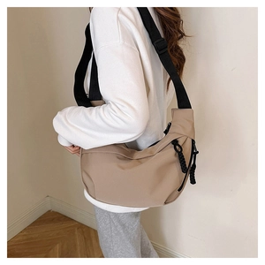 Close-up of beige crescent crossbody bag featuring adjustable black nylon shoulder strap