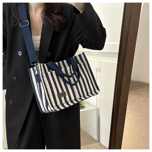 Detail of striped canvas tote bag with adjustable shoulder strap shown on a model