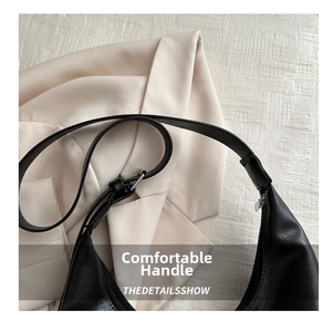 Detail of minimalist black leather shoulder bag with adjustable strap and silver metal buckle