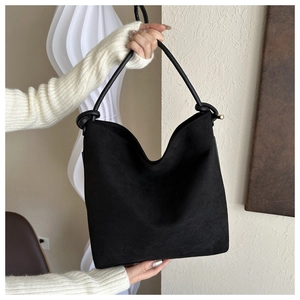 Detail of black matte suede bucket bag featuring elegant knot handle held by a model