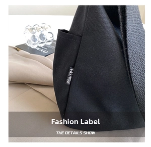 Detail shot of black canvas bag with a side pocket and a white FASHION woven label